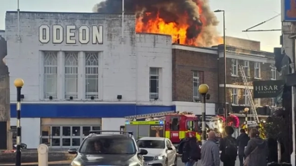 У кінотеатрі Beckenham Odeon спалахнула масштабна пожежа, внаслідок якої густий чорний дим затягнув горизонт. Пожежники одразу прибули на місце події у вівторок рано вранці, намагаючись стримати вогонь. Пожежа спалахнула о 8:15 ранку ??? Хай-стріт закрито в обох напрямках Пожежа спалахнула близько 8:15 ранку у вівторок, 30 вересня, що змусило владу перекрити Хай-стріт в обох напрямках поблизу Зе Драйв. Закриття спричиняє хаос як для місцевих жителів, так і для пасажирів. Рух автобусів порушено ??? Уникайте Хай-стріт у Бекенхемі Пожежа призвела до безладу кількох ключових автобусних маршрутів. Маршрути 54, 227, 352 та 354 перенаправлено: 54: перенаправлено від Військового меморіалу через Ректорі-роуд та Хай-стріт, реверсивний рух у тому ж напрямку. 227: об'їзд від Військового меморіалу через Ректорі-роуд, Хай-стріт та Бромлі-роуд, реверсивний рух на зворотному шляху. 352: перенаправлено з Вілледж-вей через Хай-стріт, Ректорі-роуд та Блекені-роуд, реверсивний рух назад. 354: Тепер курсує лише від Бекенхем-роуд через Ректорі-роуд. Пасажирам та водіям рекомендується уникати Хай-стріт та дотримуватися офіційних знаків об'їзду, поки аварійні бригади борються з вогнем. Десять пожежних машин та близько 70 пожежників залишаються на місці, наполегливо працюють над тим, щоб взяти полум'я під контроль. Офіційна рекомендація: уникайте району Бекенхема. Тримайте вікна та двері зачиненими, щоб запобігти вдиханню диму.