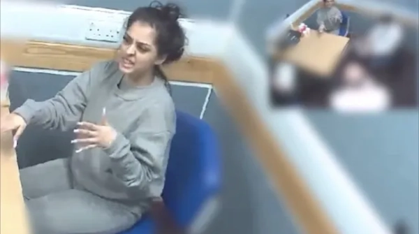 Запис з камер відеоспостереження поліції з кімнати для допитів, на якому видно молоду жінку, одягнену в сірий спортивний костюм