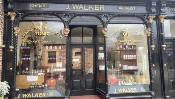 Зелено-золотий фасад магазину з написами «J Walker», «chemist» і «druggist» рекламує «тонік для нервів і мозку Квінна», «таблетки від кашлю Біча» (Beecham’s), «риб’ячий жир доктора Брукса» та «заспокійливі порошки».