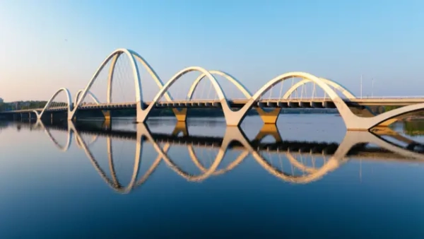 Фотографія сучасного мосту з кількома вигнутими краями, що відбиваються у воді 
