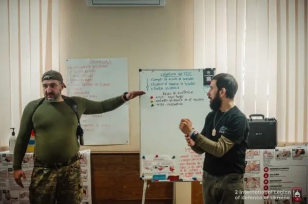 Два чоловіки стоять біля дошки і показують на неї