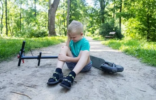 Малолітній хлопчик сидить біля поваленого на землю електросамоката й витирає сльози на обличчі. 