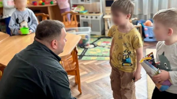 Дорослий чоловік сидить, пригнувшись, біля дітей у дитсадку