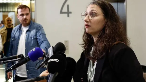 A woman called Elisabeth Guthmann wearing a dark coat and glasses talks into microphones