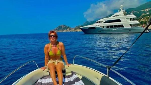 Кершоу сидить на носі човна, повернувшись спиною до моря. Позаду — велика яхта та берегова лінія