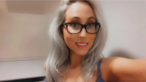 Self-portrait of a young woman wearing glasses with long blonde hair; a close-up of her face taken indoors against a neutral light background.