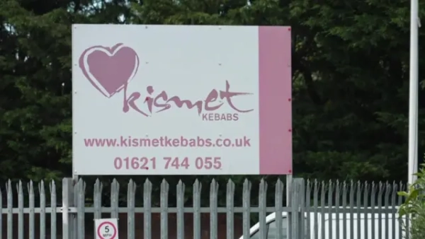 Біло-рожева зовнішня вивіска Kismet Kebabs над металевою огорожею.