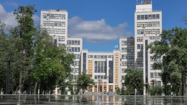 Будівля Держпрому, оточена деревами, з фонтаном на передньому плані. Фото зроблене вдень за ясної погоди.