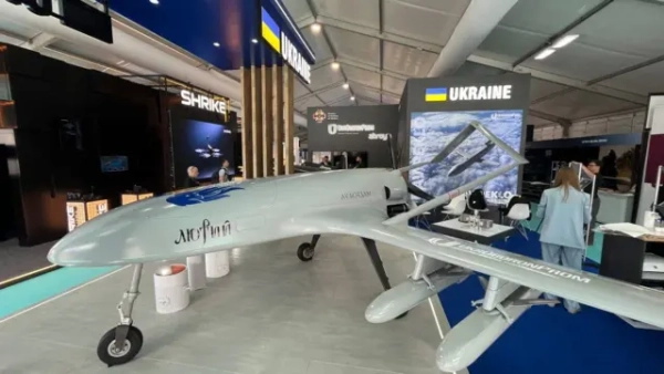 Безпілотник "Лютий", представлений на українському стенді авіасалону у Фарнборо. Експонат розміщений у павільйоні "Укроборонпрому" на тлі української експозиції з державними прапорами та стендами оборонних компаній