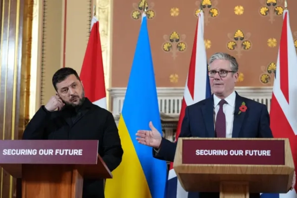  Зеленський і Стармер виступають на заході, позаду них прапори Великої Британії та України, на стендах написано Securing our future.
