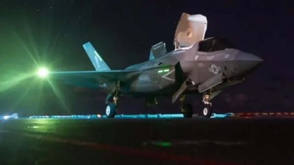 Сучасний військовий винищувач F-35, що стоїть на злітній смузі вночі. Літак освітлений зеленими та білими вогнями, кабіна закрита, шасі випущене.