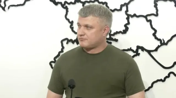 Чоловік у темнозеленій футболці перед мікрофоном 
