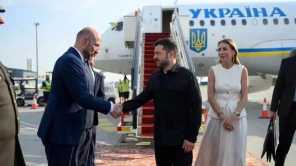 Зеленський тисне руку чоловіку, біля них стоїть жінка. На тлі - великий літак з написом "Україна"