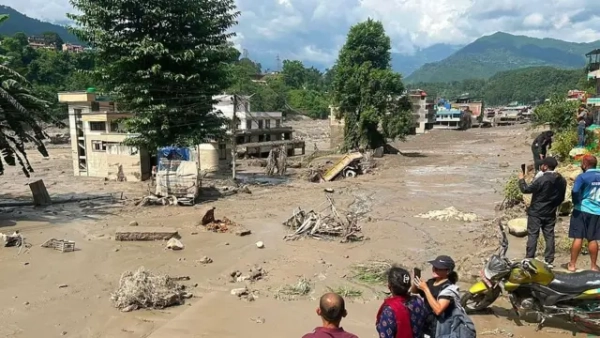 Повні води та бруду вулиці, кілька людей стоять на узбіччі та знімають те, що відбувається на телефон.