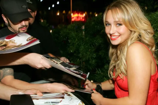 Гейден Панеттьєр під час вечірки Teen Vogue Young Hollywood на червоній доріжці роздає автографи. Вона одягнена в червону сукню та усміхається в камеру.