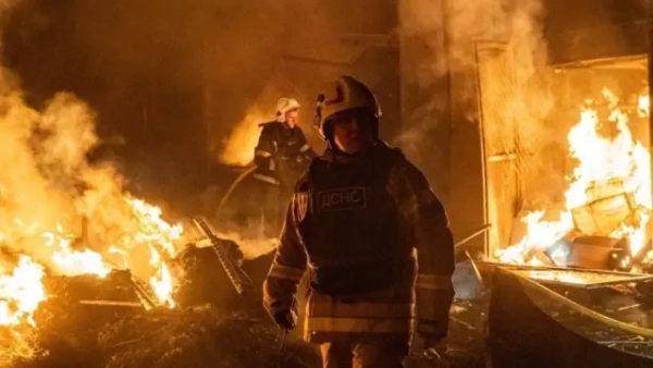 Рятувальники працюють серед масштабної пожежі вночі: навколо палають уламки та будівельні конструкції, приміщення охоплене полум’ям і густим димом. На передньому плані рятувальник у захисному спорядженні, на задньому видно інших пожежників, які гасять вогонь.