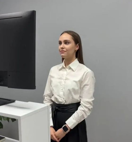 Ведуча онлайн-церемонії Богдана Олех у білій сорочці та чорній спідниці стоїть перед монітором